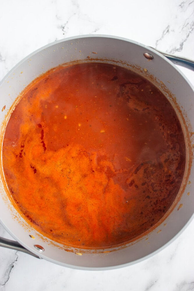 A pot filled with simmering red tomato-based sauce sits on a white marble surface.