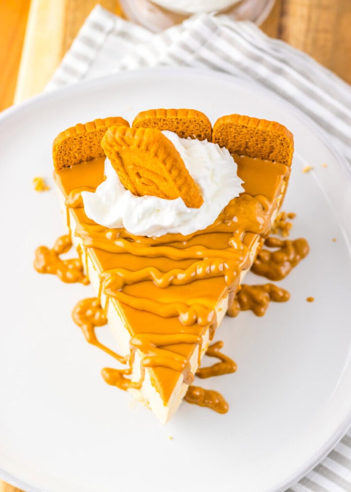 A slice of cheesecake topped with caramel sauce, whipped cream, and three cookie pieces on a white plate.