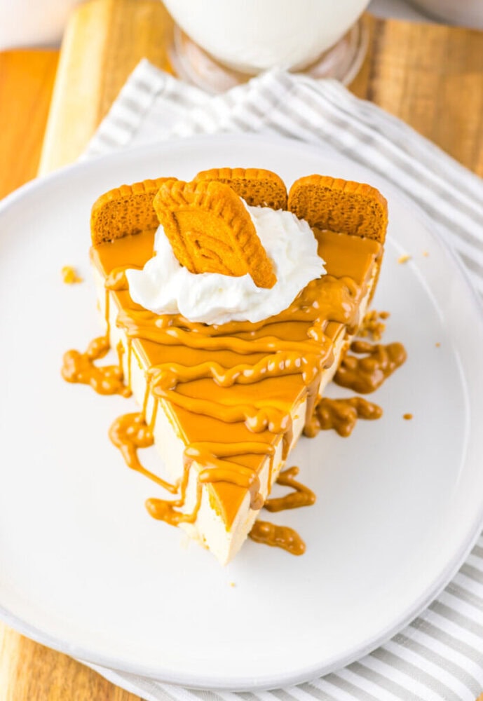 A slice of cheesecake topped with caramel drizzle, whipped cream, and three rectangular cookies on a white plate.