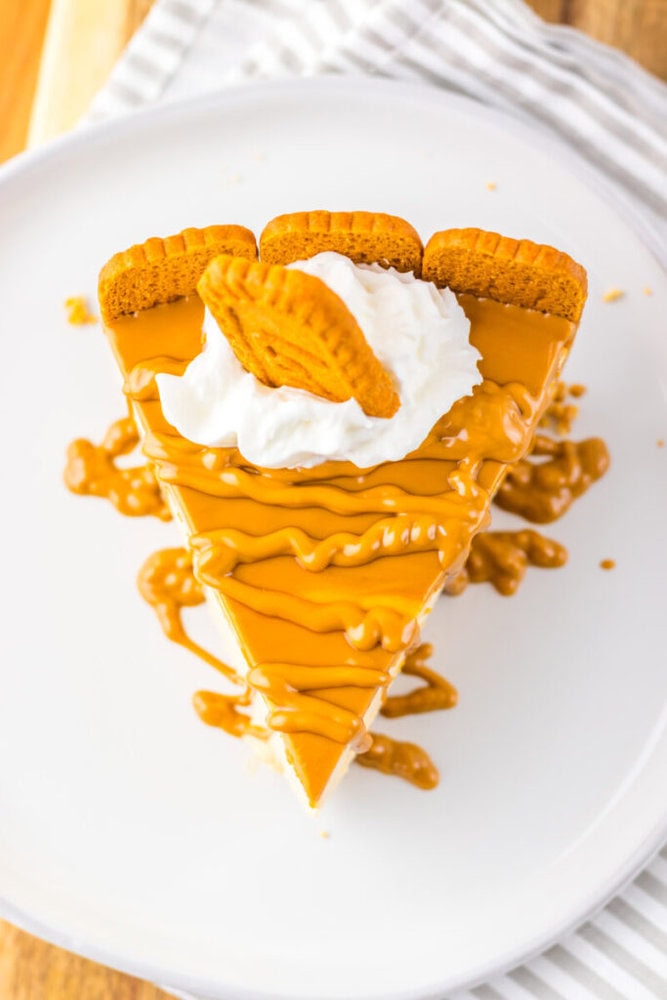 A slice of caramel-drizzled pie topped with whipped cream and two cookies, served on a white plate.