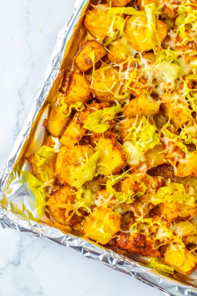 Sliced roasted potatoes topped with melted cheese and sliced yellow peppers on a foil-lined baking sheet.