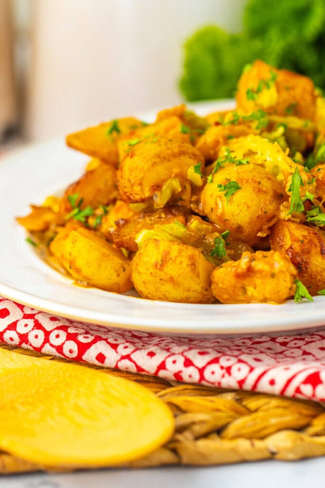 A white plate filled with seasoned roasted potatoes and garnished with chopped herbs, sits on a red patterned napkin.