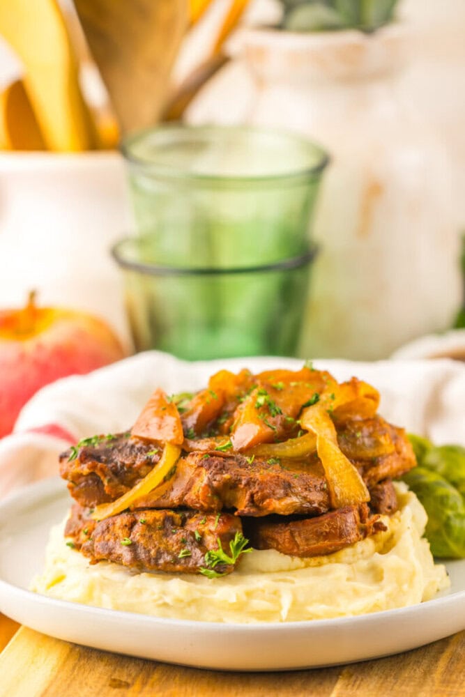 Braised beef with sautéed onions served on a bed of mashed potatoes, garnished with herbs.