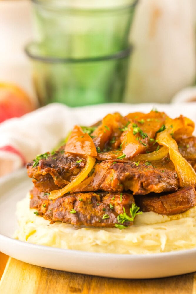 A plate of mashed potatoes topped with cooked beef patties, sautéed onions, and peppers, garnished with chopped herbs.
