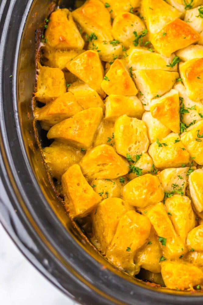 Golden biscuit pieces baked in a slow cooker, topped with melted cheese and garnished with chopped parsley.