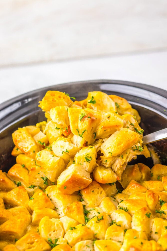 A spoon lifts a serving of golden, baked biscuit pieces topped with herbs from a dish.