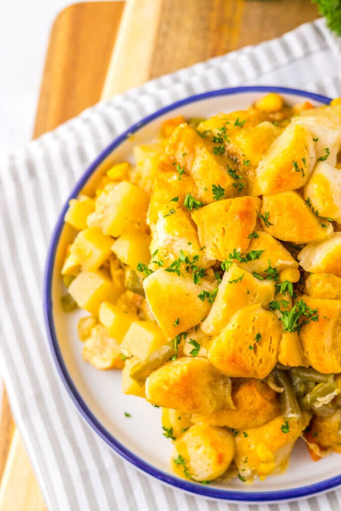 A plate of baked casserole topped with golden biscuit pieces, mixed with vegetables and garnished with chopped herbs, on a striped cloth.