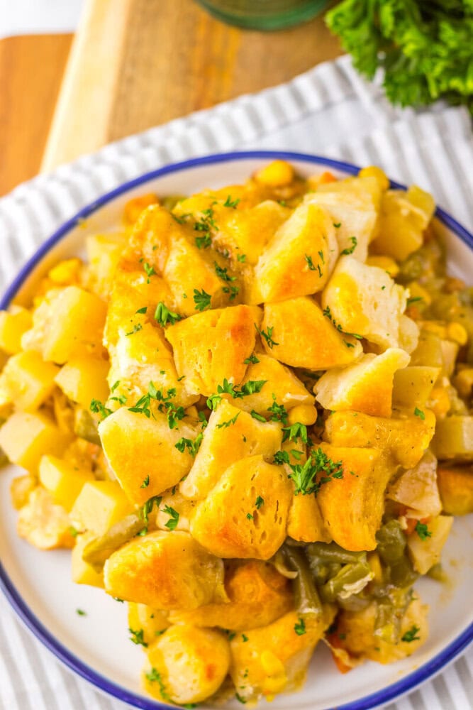 A plate of chicken and vegetable casserole topped with golden biscuit pieces and sprinkled with chopped parsley.