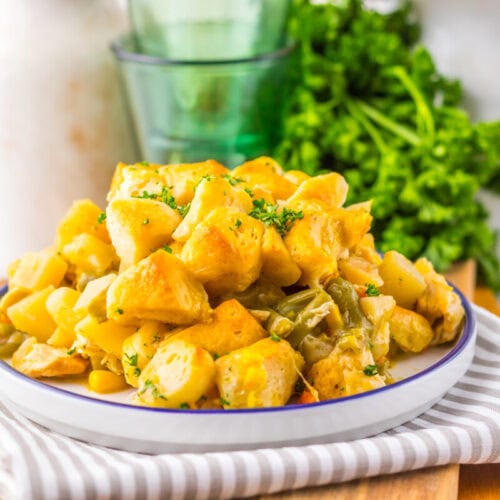 A plate of cooked cubed potatoes garnished with herbs, placed on a striped cloth with parsley and glassware in the background.