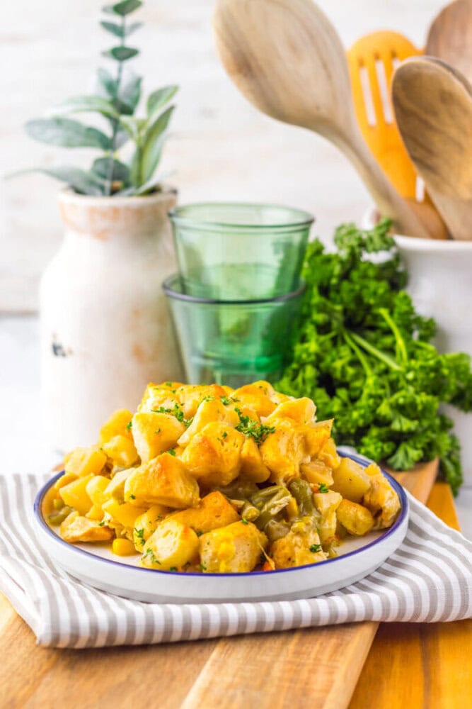A plate of seasoned cubed potatoes with herbs sits on a striped napkin, with parsley, green glasses, and wooden utensils in the background.