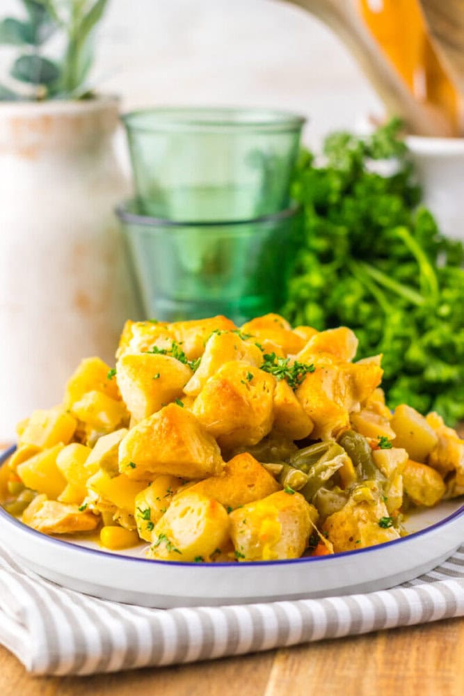A plate of creamy yellow potato and vegetable casserole garnished with chopped herbs, placed on a striped napkin with green glasses and fresh parsley in the background.
