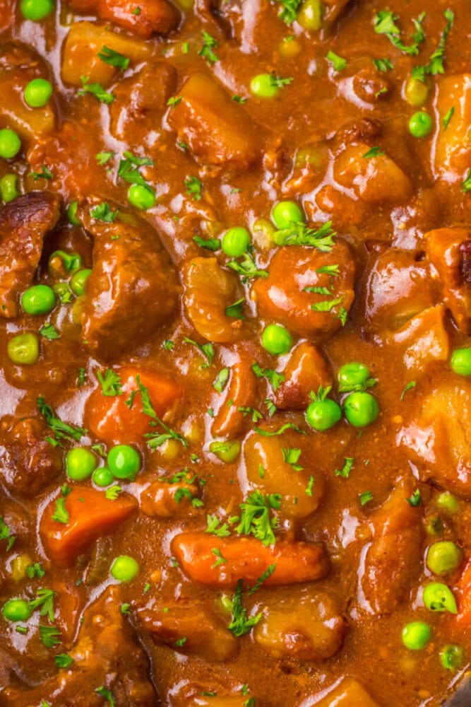 Close-up of beef stew with chunks of beef, carrots, peas, potatoes, and a thick brown gravy, garnished with chopped parsley.