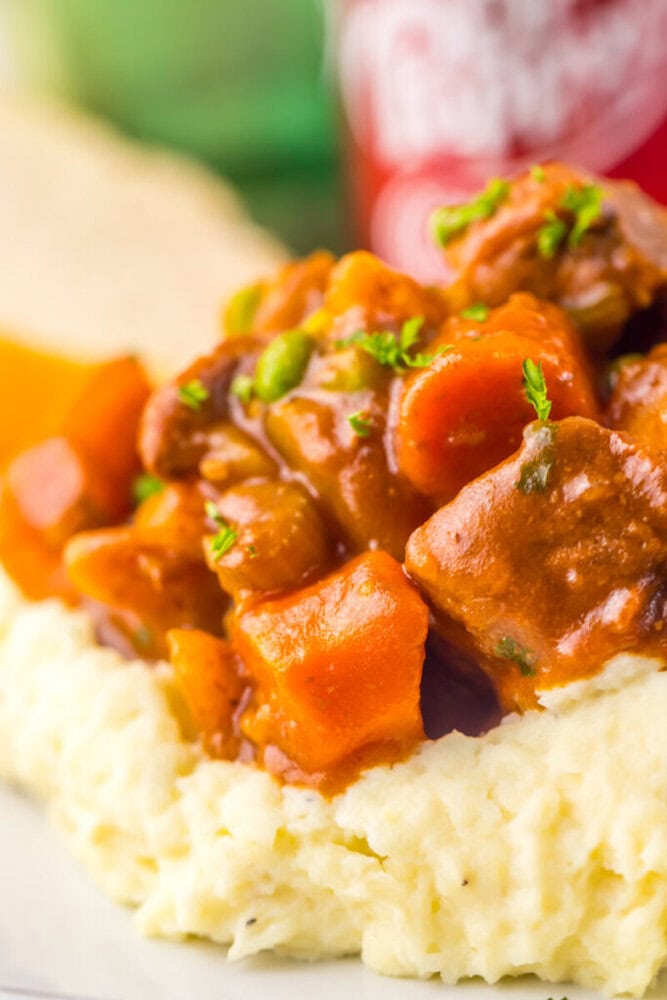 Close-up of beef stew with carrots and peas served over mashed potatoes, garnished with parsley.