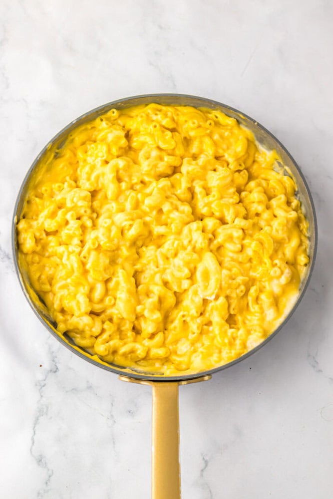 A pan filled with creamy macaroni and cheese sits on a white marble surface.