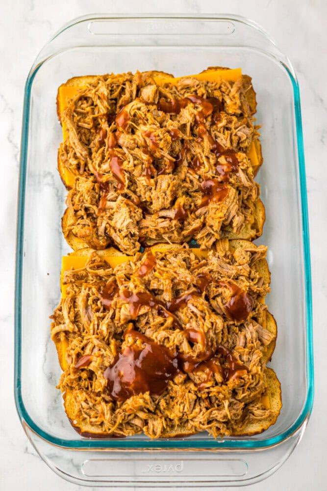 A glass baking dish with four slices of bread topped with shredded barbecue chicken and sauce.