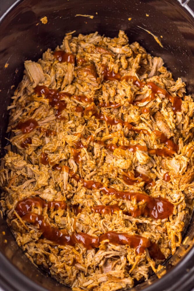 Shredded barbecue chicken with sauce drizzled on top in a slow cooker.