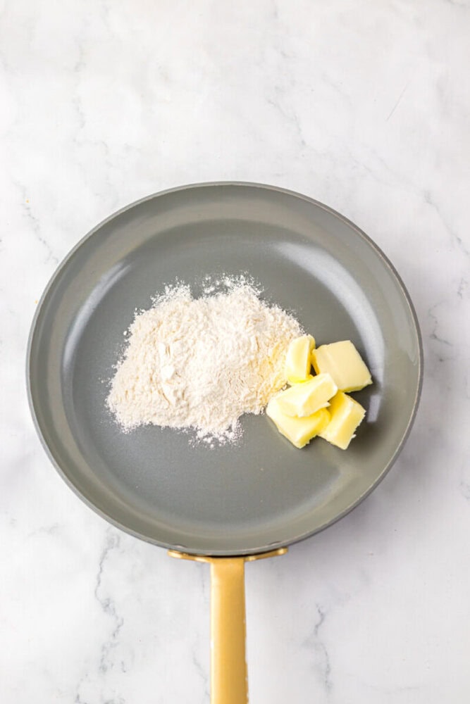 Nonstick pan with a pile of flour and several cubes of butter on a white marble surface.