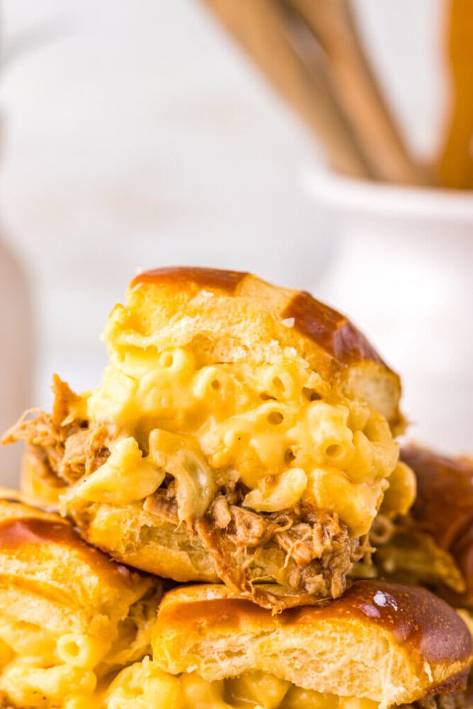 A close-up of a sandwich with pulled pork and macaroni and cheese on a pretzel bun, stacked on top of similar sandwiches.