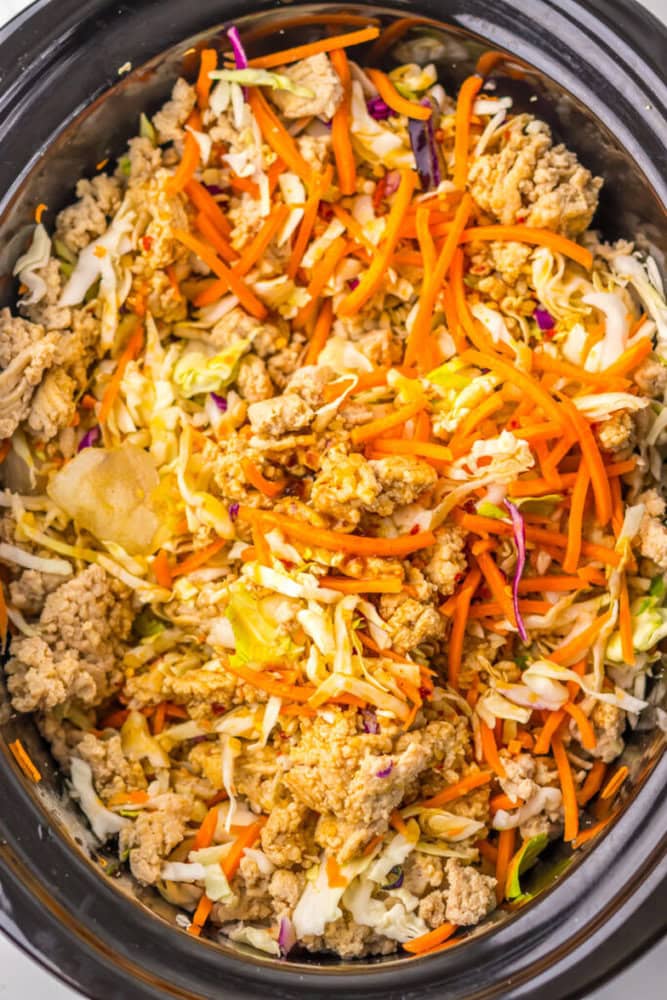 A close-up of a slow cooker filled with cooked ground meat, shredded cabbage, and julienned carrots.