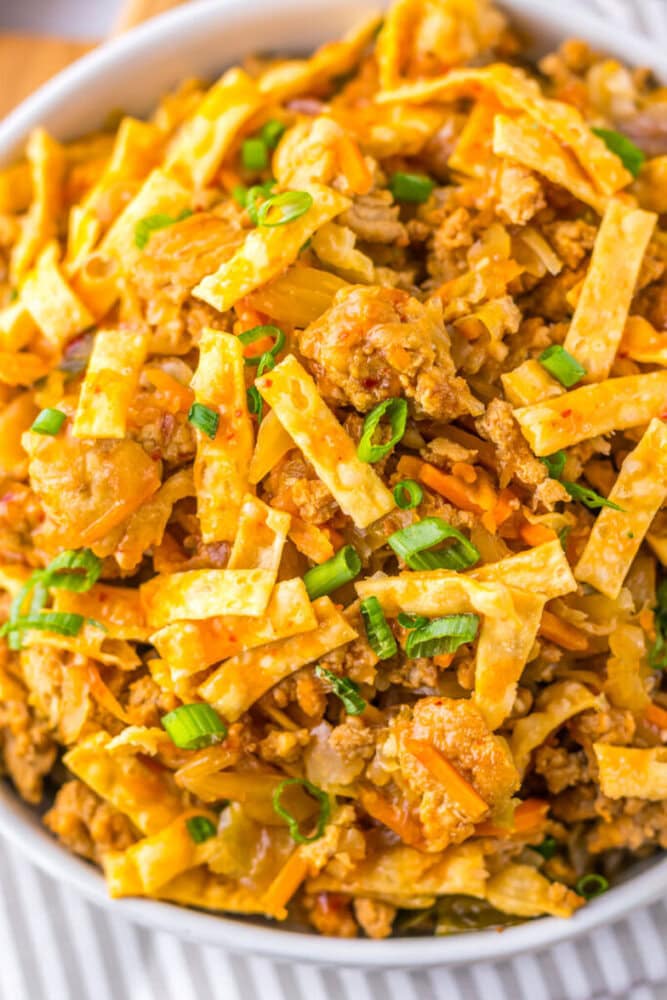 A close-up of an egg roll in a bowl dish with ground meat, shredded vegetables, sliced wonton strips, and chopped green onions.