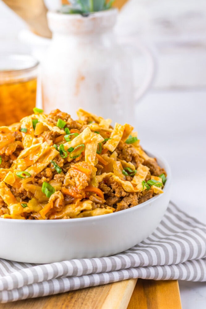 A white bowl filled with an egg roll in a bowl dish, featuring ground meat, cabbage, and green onions, sits on a striped napkin.