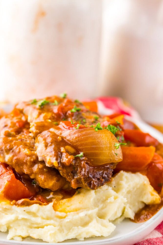 A plate of mashed potatoes topped with Salisbury steak, onions, and red bell peppers in brown gravy.
