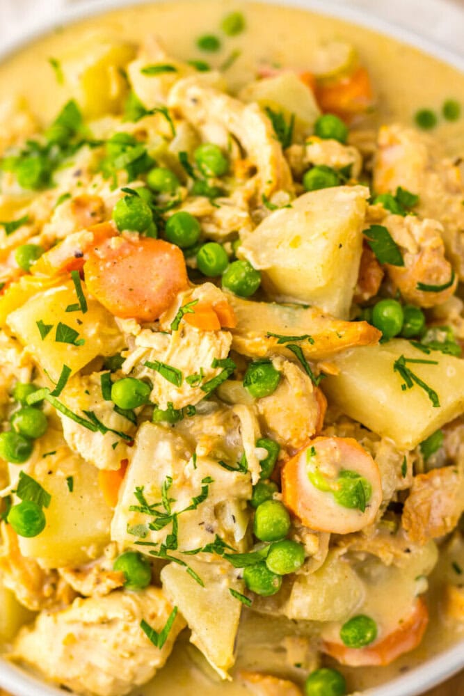 A close-up of a chicken and vegetable stew with carrots, peas, potatoes, and herbs in a creamy sauce.