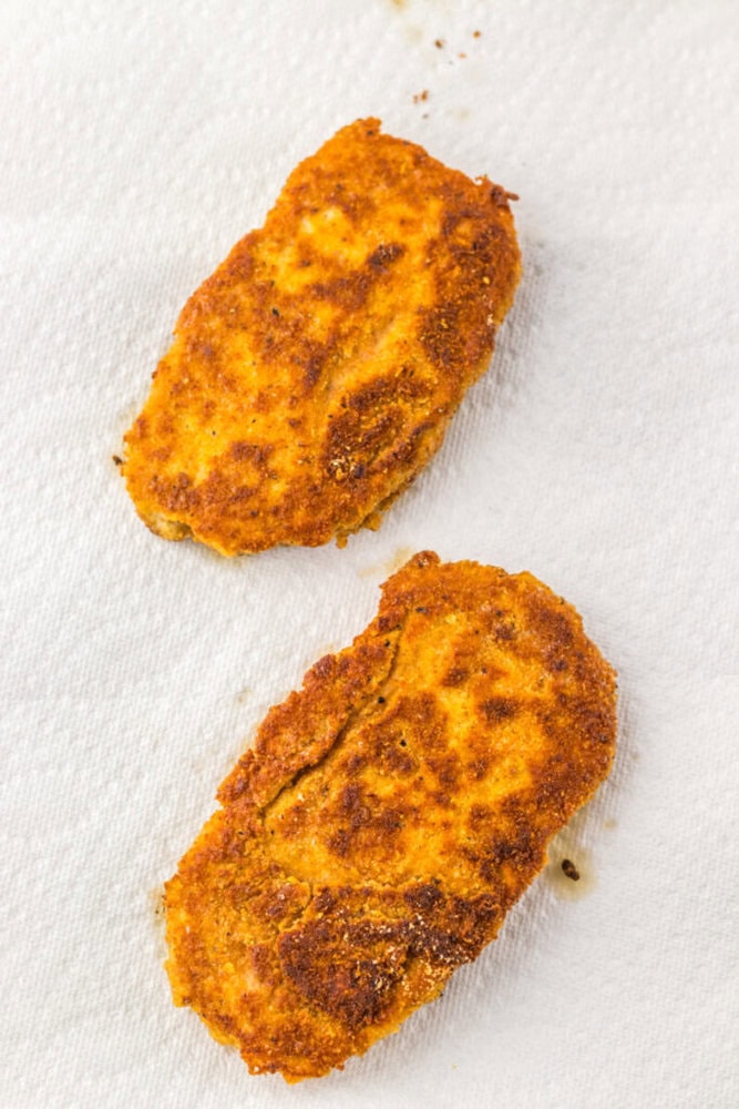 Two breaded and fried cutlets resting on a white paper towel to absorb excess oil.