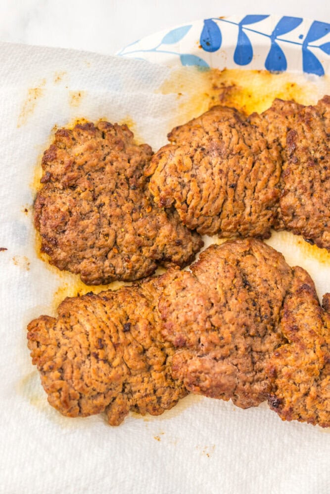 Four fried pieces of breaded meat rest on a paper towel to absorb excess oil, placed on a patterned plate.