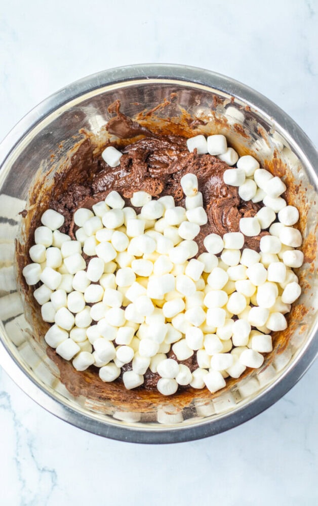 A metal mixing bowl containing chocolate batter and a pile of mini marshmallows on top, ready to be mixed together.