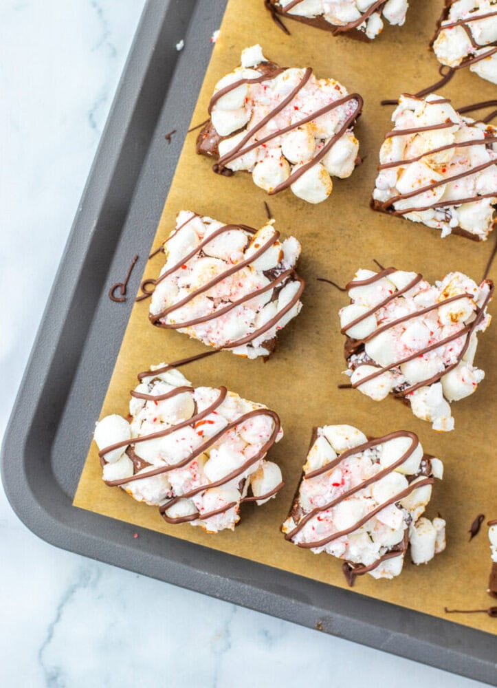 Squares of popcorn clusters drizzled with chocolate are arranged on parchment paper on a baking tray.