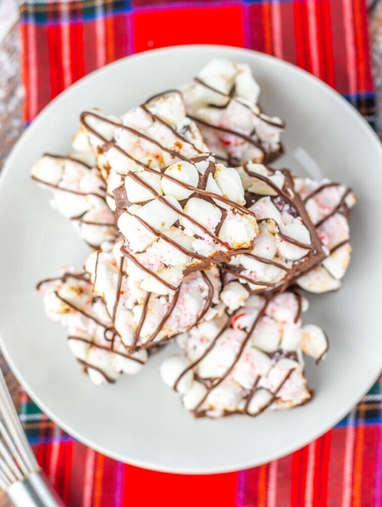 A plate of white chocolate peppermint bark pieces drizzled with dark chocolate, placed on a red plaid cloth.