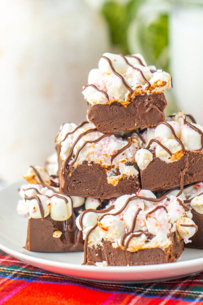 A plate of chocolate fudge squares topped with mini marshmallows, crushed peppermint, and drizzled with chocolate.