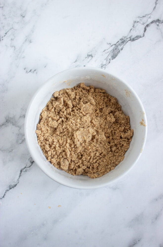 A white bowl filled with crumbly brown mixture sits on a white marble surface.