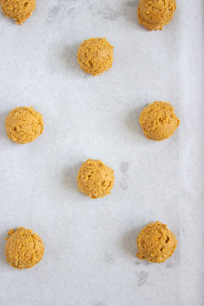 Scoops of cookie dough are evenly spaced on a parchment-lined baking sheet, ready for baking.