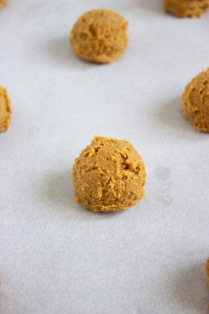 A scoop of unbaked cookie dough sits on a sheet of parchment paper, with other dough portions spaced around it.