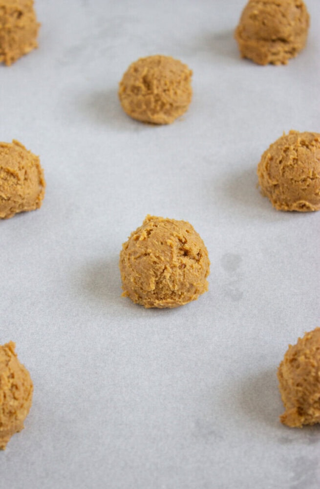 Scoops of cookie dough spaced evenly on a baking sheet lined with parchment paper, ready for baking.