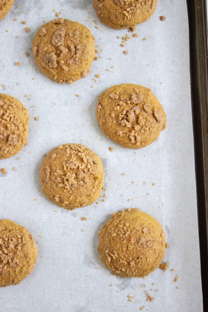 Round, golden-brown cookies with crumbly topping are arranged on a parchment-lined baking sheet.