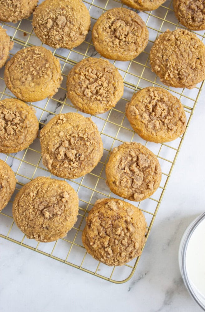 A cooling rack with pumpkin muffins topped with crumbly streusel, arranged on a white marble surface.