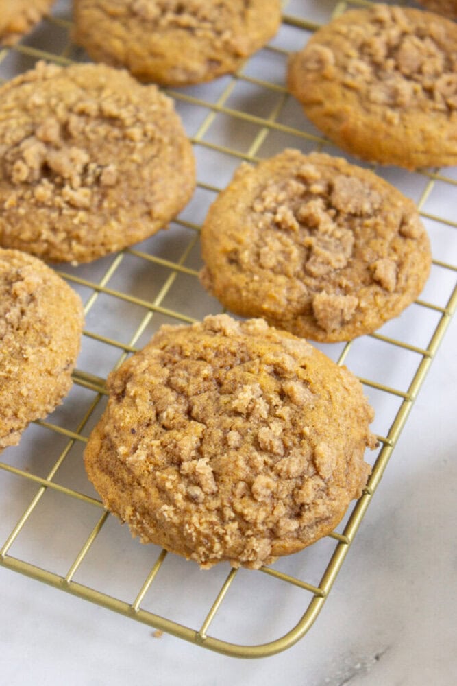 Several crumb-topped cookies are cooling on a metal wire rack placed on a white surface.