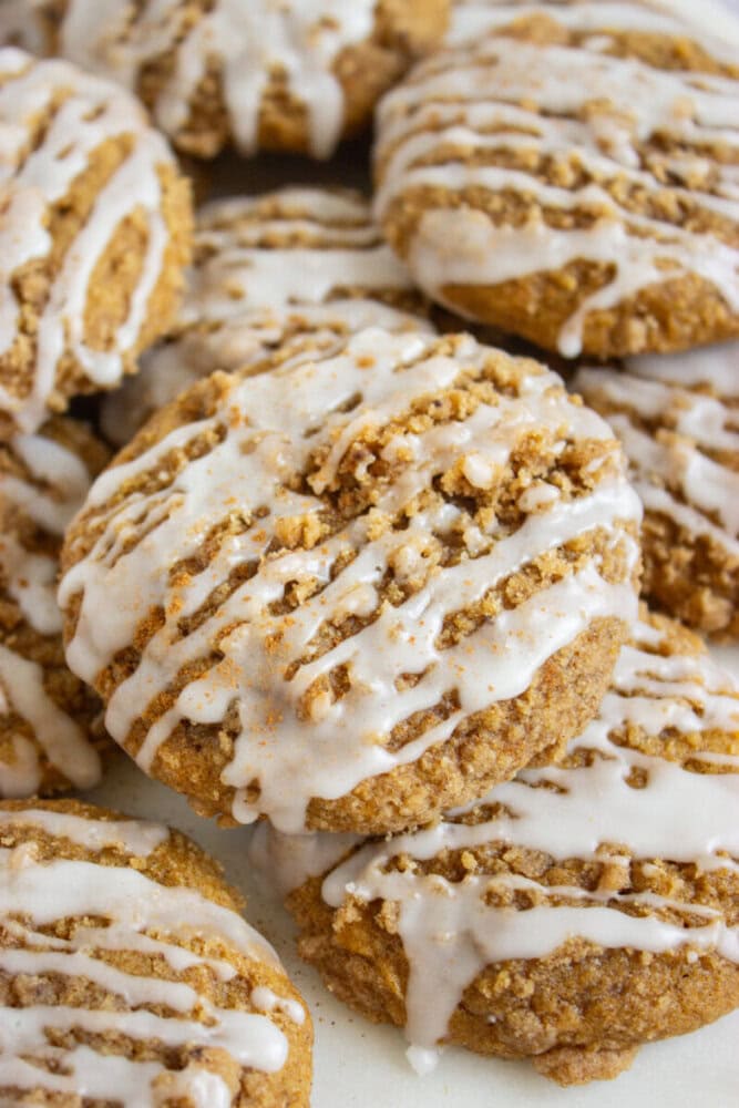 Close-up of several pumpkin cookies topped with white icing drizzle and crumbly streusel.