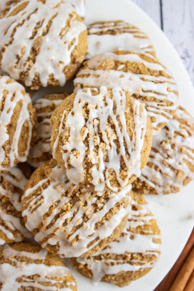 A close-up of several round cookies topped with white icing drizzle, arranged on a white plate.