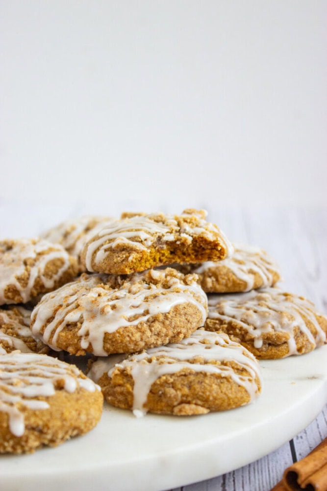 A plate of crumb-topped cookies with white icing drizzle, one cookie broken in half to show the inside.