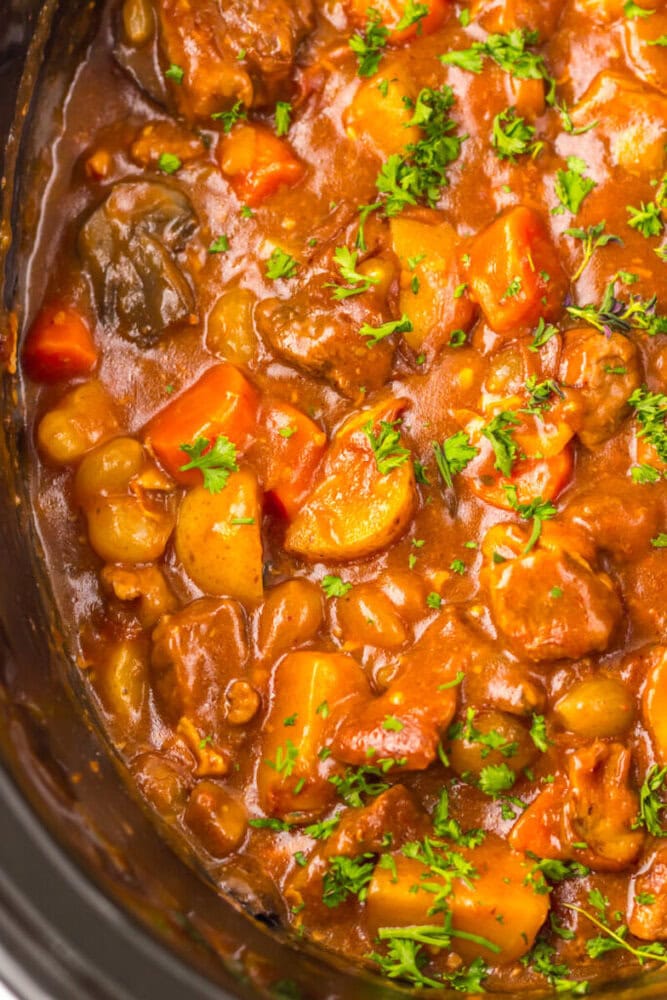 Close-up of beef stew with carrots, potatoes, peas, and chopped parsley in a thick, rich sauce.