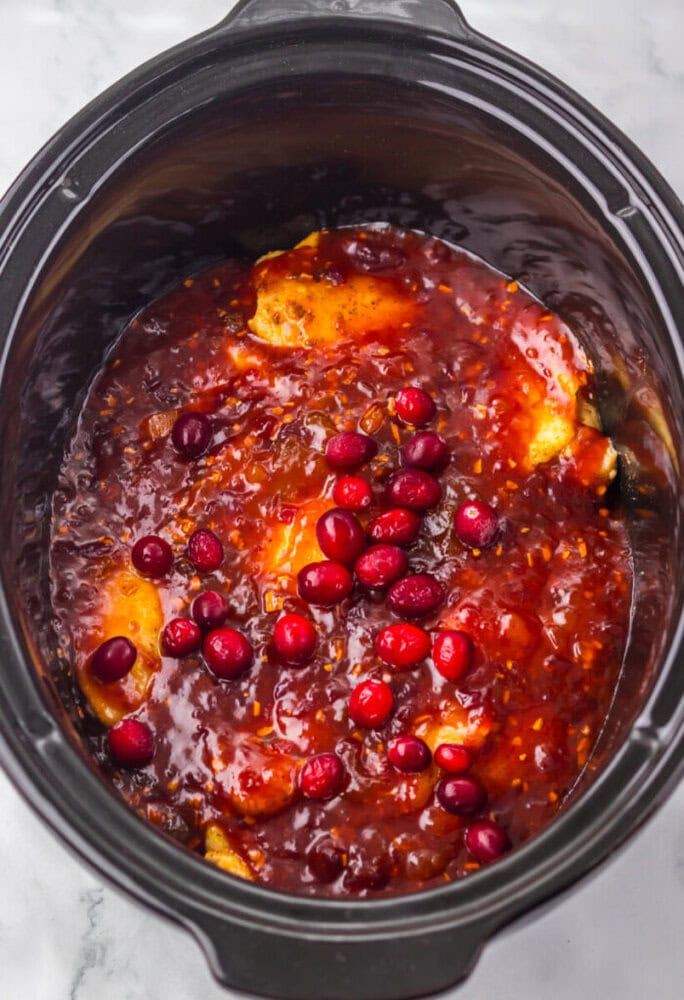 Boneless chicken breasts in a slow cooker covered with cranberry sauce, whole cranberries, and orange glaze.