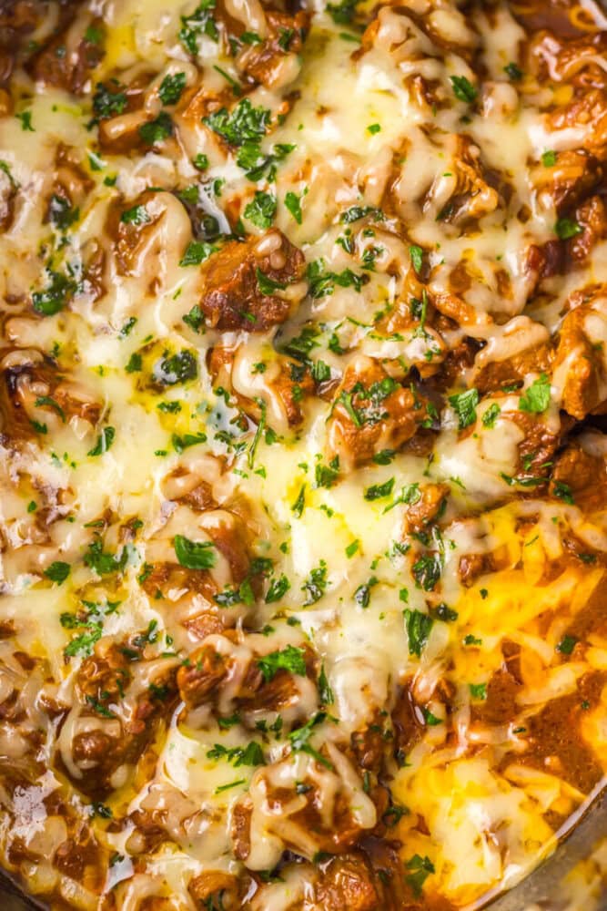 Close-up of shredded beef in sauce topped with melted cheese and chopped parsley.