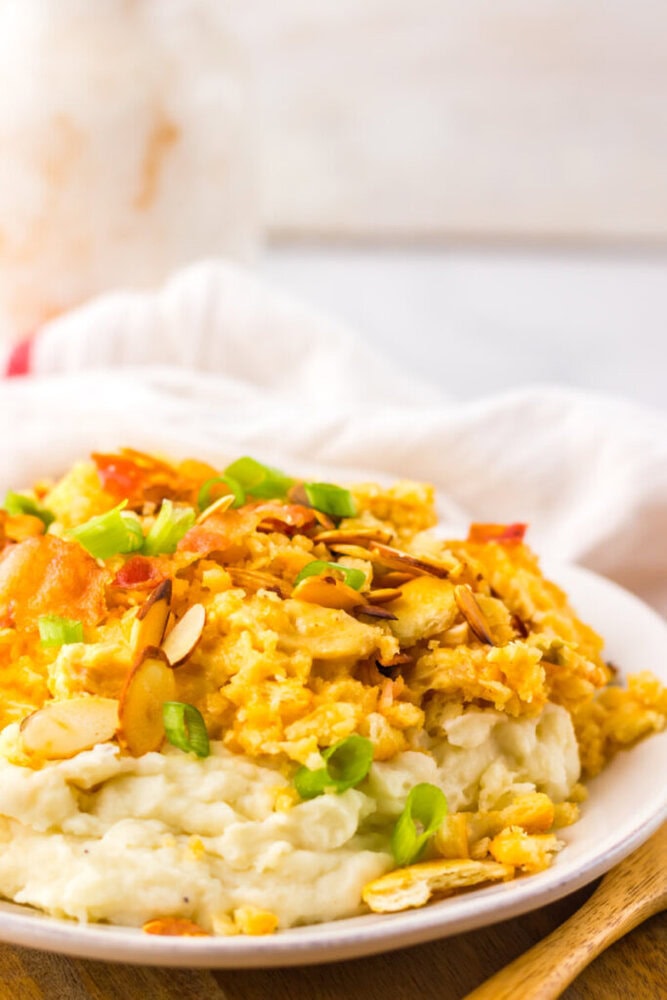 A plate of mashed potatoes topped with scrambled eggs, sliced almonds, chopped green onions, and small pieces of red bell pepper.