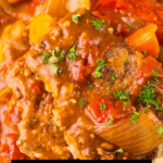 A plate of Swiss Steak cooked in a slow cooker with onions, carrots, and tomatoes, garnished with parsley.