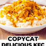 A bowl of mashed potatoes topped with fried chicken pieces, corn, shredded cheese, and brown gravy.