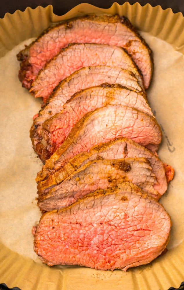 Several slices of medium-rare roast beef arranged in a single layer on brown parchment paper.